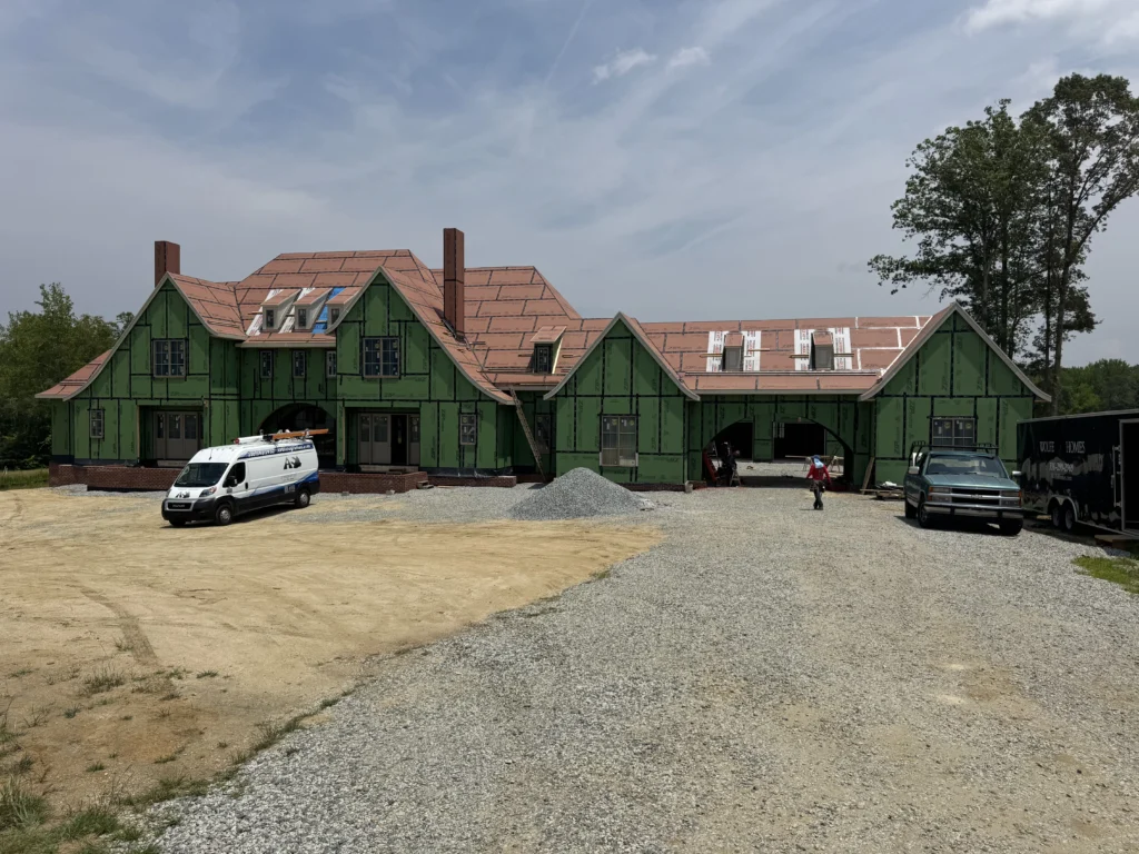 A photo of a new home construction site featuring a large green-framed house under construction, with a tiled roof and dormer windows.