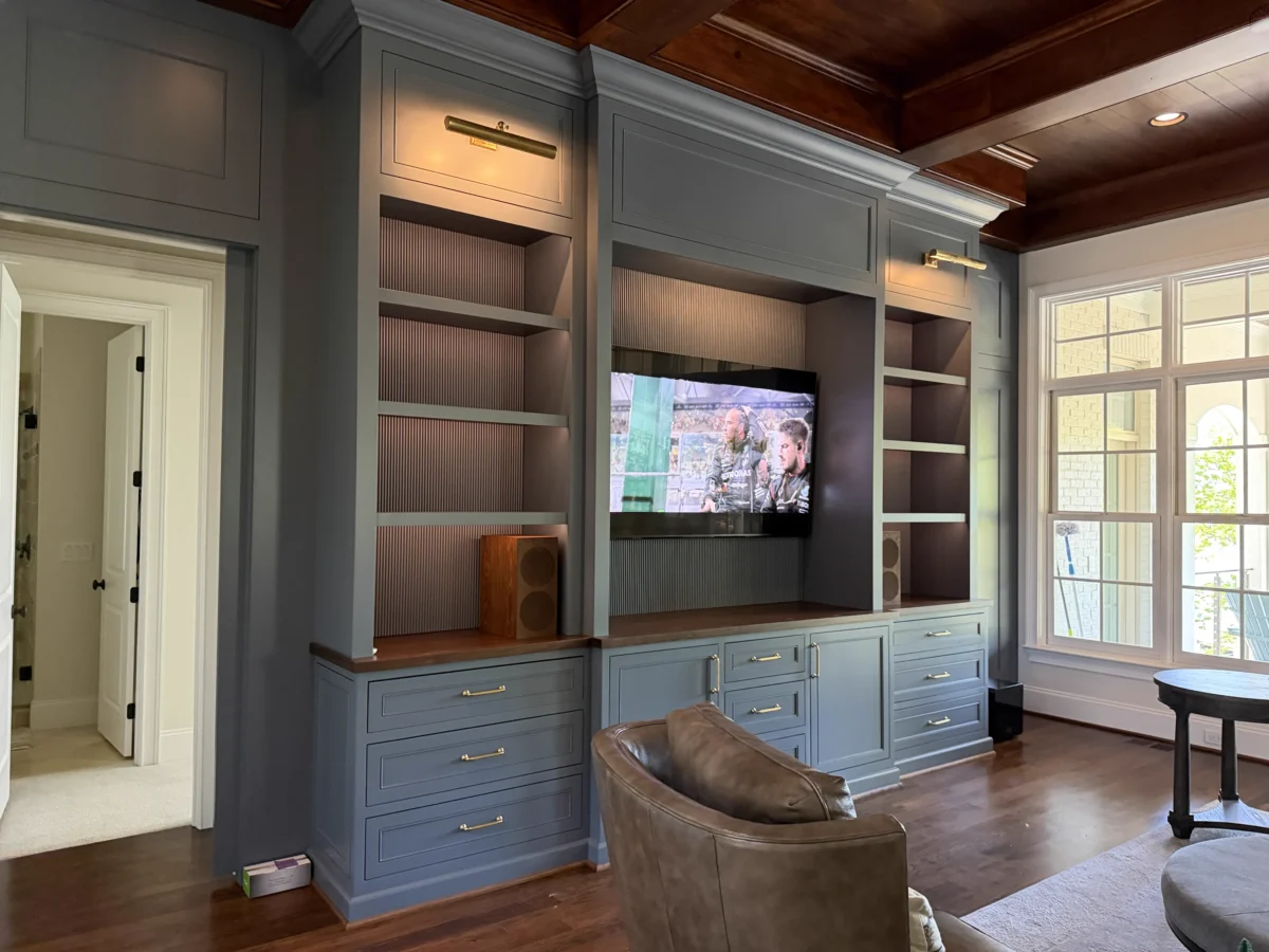 Close-up of the custom-built entertainment center featuring hidden TV lift mechanism, warm cove lighting, fluted paneling, and integrated speakers in a sophisticated blue-gray finish.